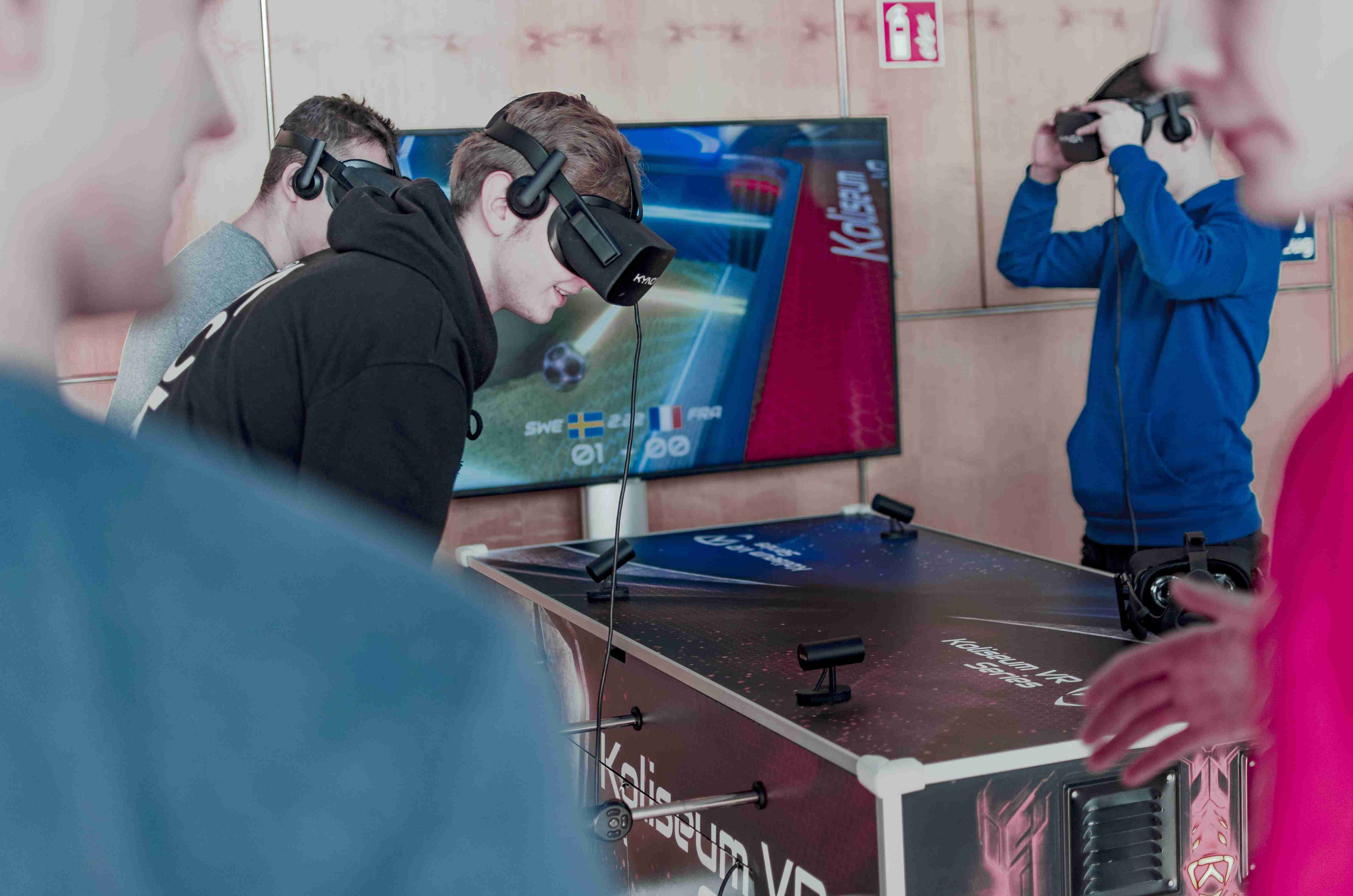 Mehrere Menschen bedienen einen Kicker und haben VR-Brillen auf